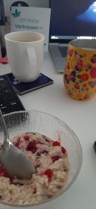 Porridge, Tee- und Kaffeetasse stehen auf dem Schreibtisch neben der Tastatur